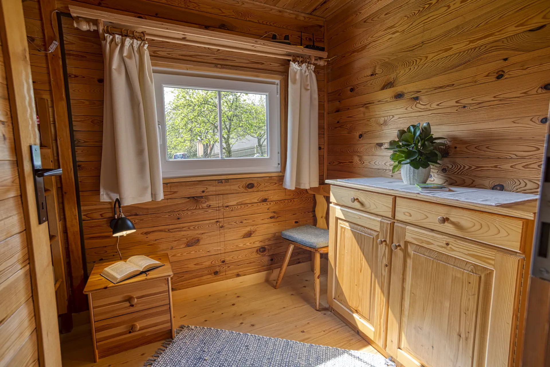 Leseecke im Dreibettzimmer mit Fenster, Kommode und Buch auf Nachttisch